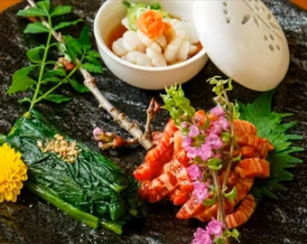 黒い石板の上に花や葉で飾り付けられた前菜と蒸し碗が盛られた写真
