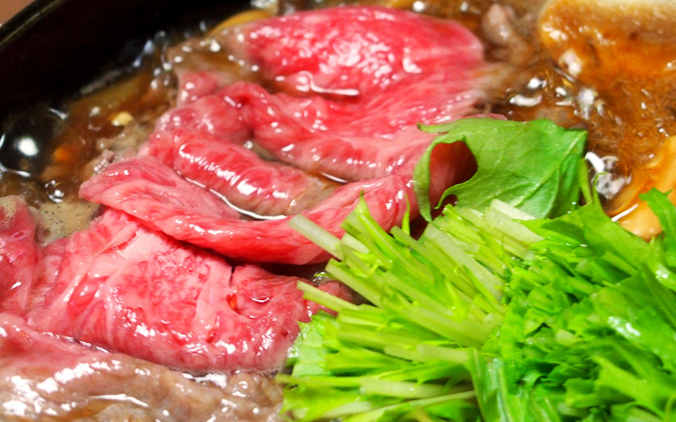 霜降り和牛と水菜が煮えるすき焼きのアップの写真